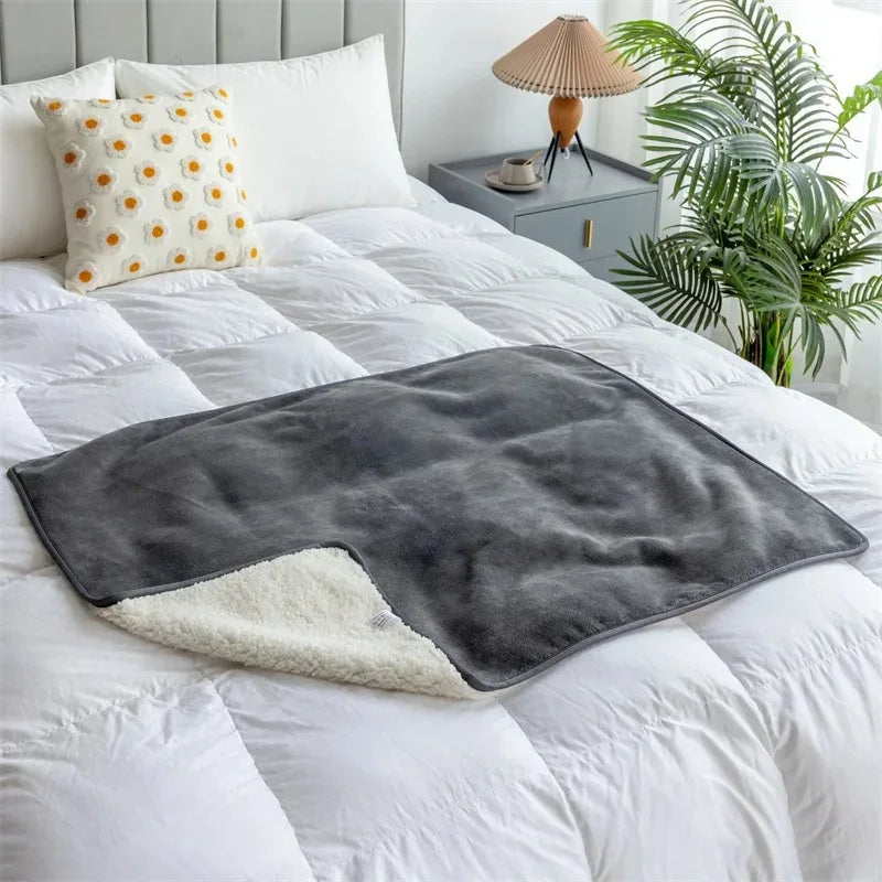 The Everywhere Blanket in Gray with its sherpa-style reverse folded back on a white bed.