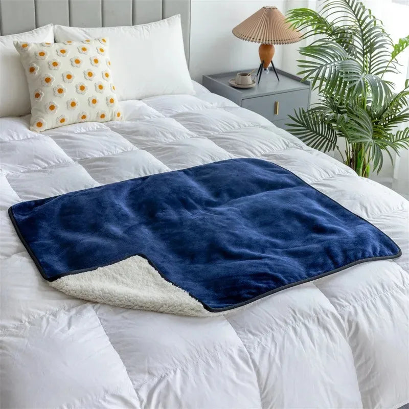 The Everywhere Blanket in Blue with its sherpa-style reverse on a white bed.